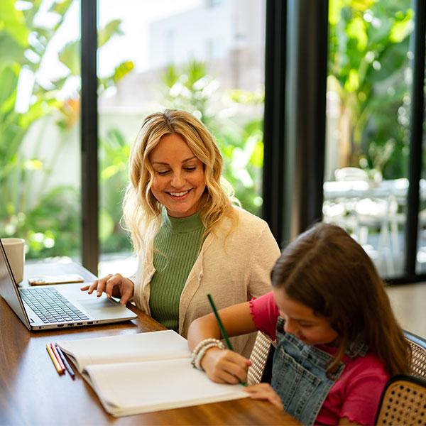 Une mère travaille sur son ordinateur portable pendant que sa fille dessine à côté d'elle.